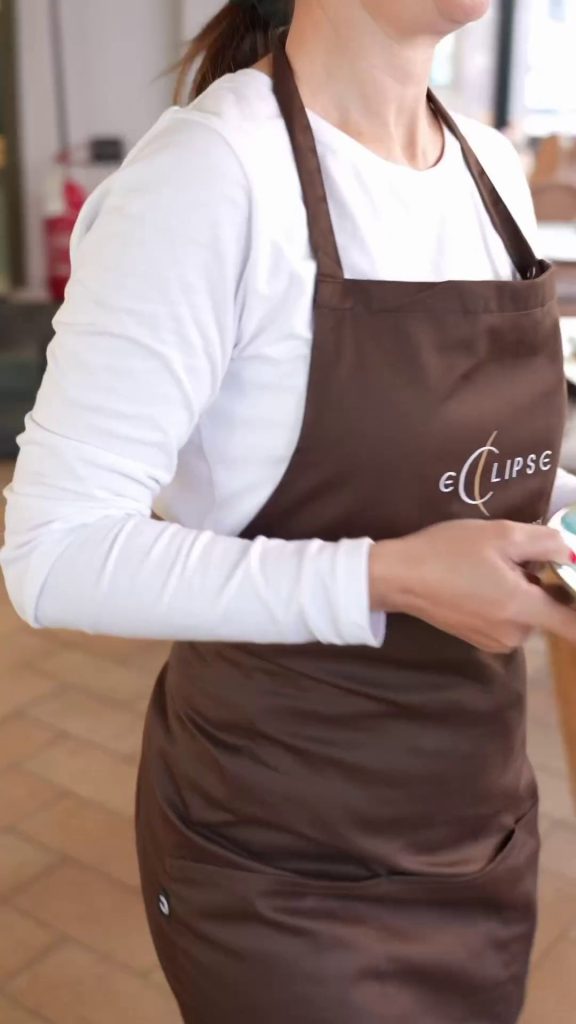 La cameriera con grembiule cacao corto e maglietta bianca a maniche lunghe tiene un piatto