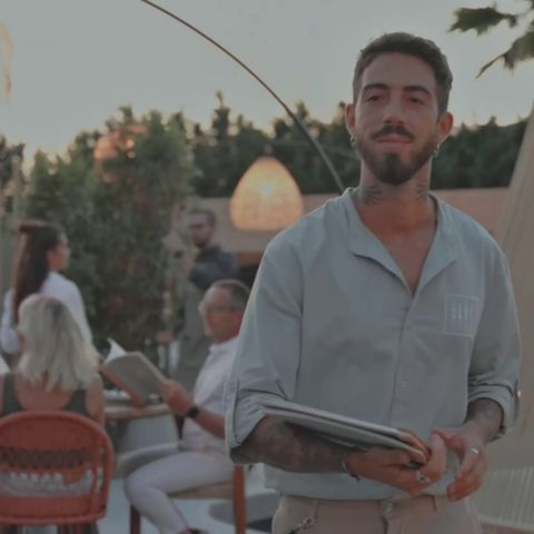 Cameriere tatuato in piedi davanti a un tavolo indossa una divisa personalizzata per la Churrascheria Agua di Alghero, realizzata da Raimonda Lai.