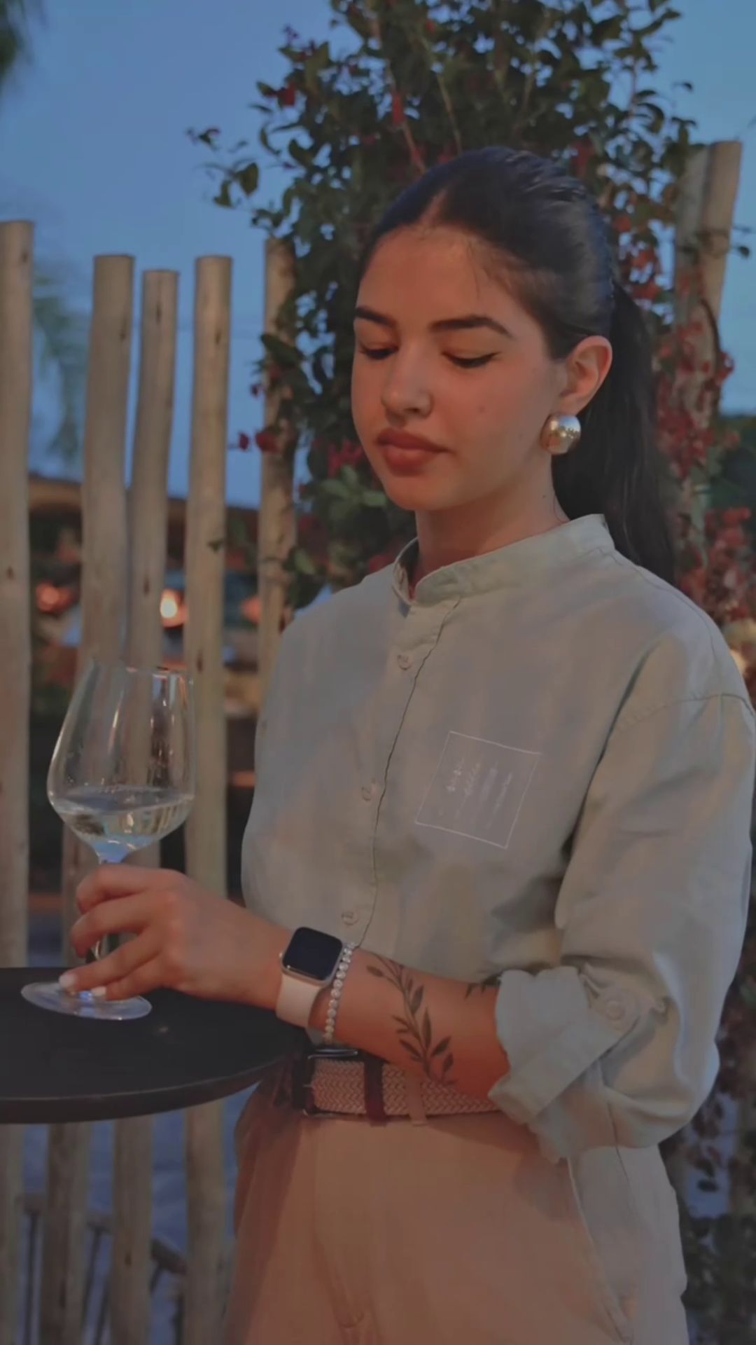 Cameriera in piedi all'esterno della churrascheria Agua con un bicchiere di vino, vestita con un abito personalizzato da Raimonda Lai.